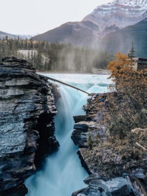 Breathtaking view of Athabasca Falls cascading in Jasper National Park with mountains and autumn foliage.